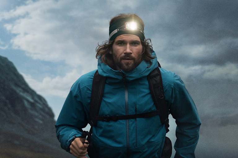 Ein Mann mit einer leuchten Stirnlampe geht mit Wanderausrüstung