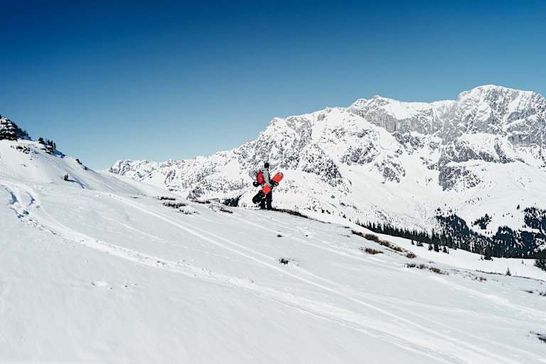Ein Snowboarder steht in der Winterlandschaft mit Blick auf den Hochkönig.
