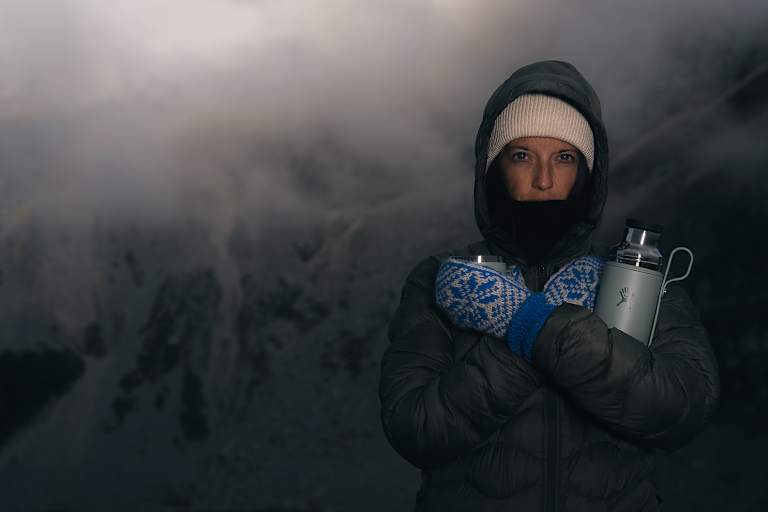 Person in Winterkleidung mit Thermosflasche Hydro Flask Hot Flask & Cup in verschneiter Berglandschaft bei Nebel und eisigen Temperaturen.