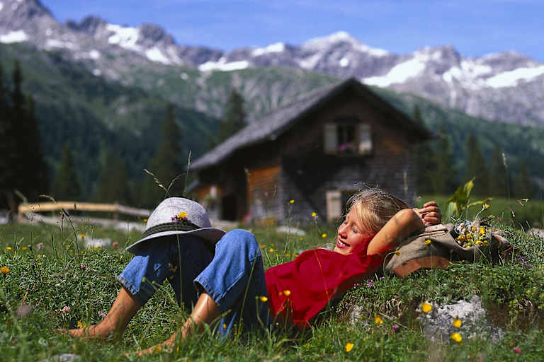 Mädchen auf einer Almwiese mit Berghütte im Hintergrund