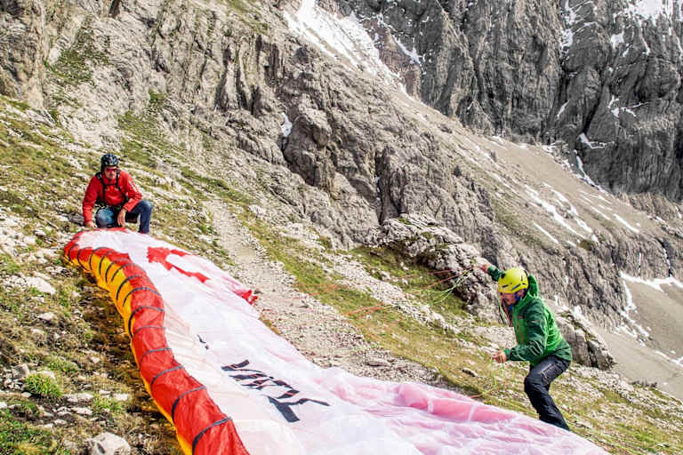 Der Tandemschirm wird vorbereitet, im Hintergrund ist eine mächtige Felswand zu sehen