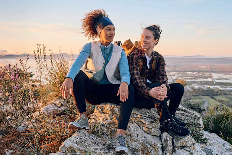 Zwei Frauen sitzen auf einem Fels in den Bergen.