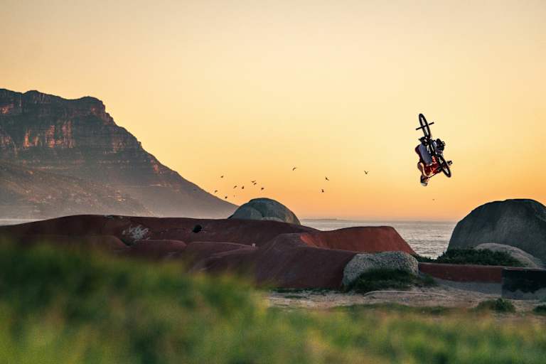 BMX-Biker dreht sich in Luft vor Küstenszenerie.