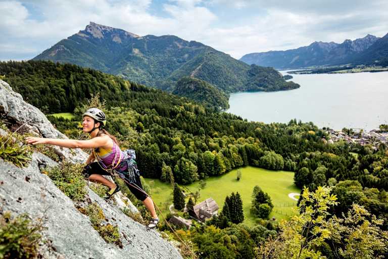 Manuela klettert am Plombergstein, im Hintergrund der türkise Wolfgangsee