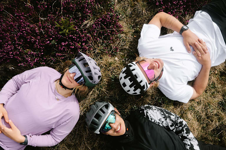 Drei junge Männer mit Helmen von Alpina liegen in der Wiese.
