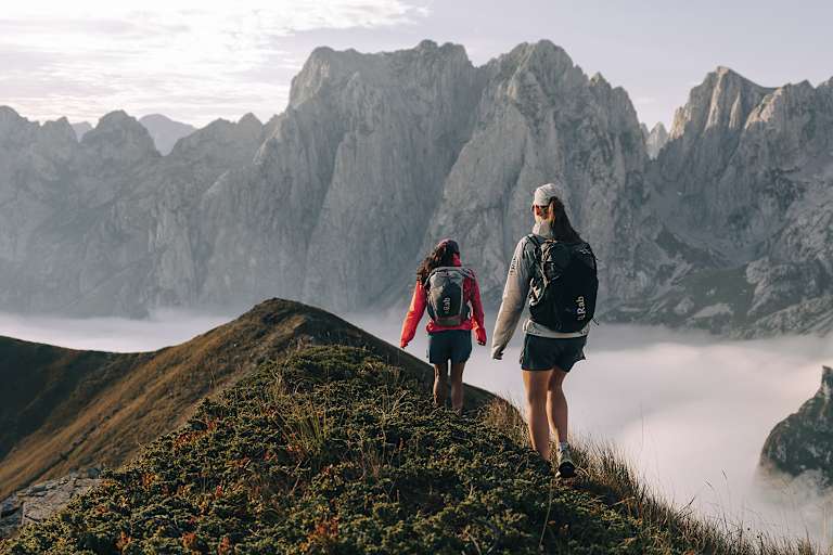 Zu sehen sind zwei Personen die einen felsigen Berg empor steigen und Rucksäcke von Rab tragen.