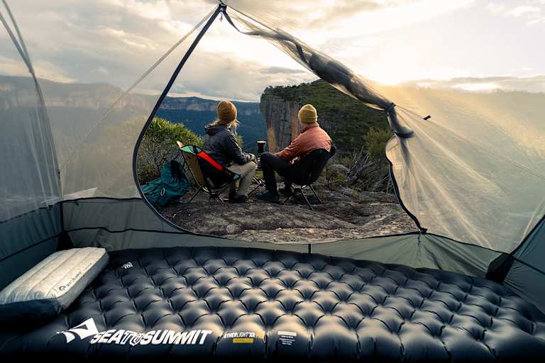 Sea to Summit Isomatte und Kissen im Zelt mit Blick auf zwei Camper, die den Sonnenuntergang in den Bergen genießen