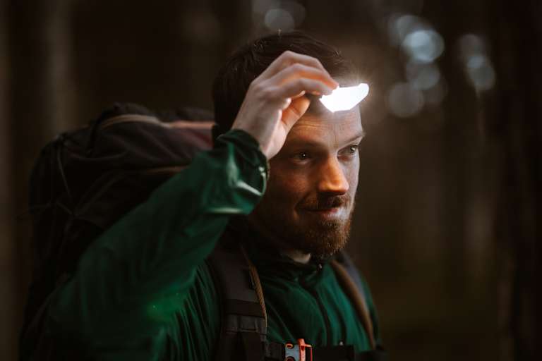 Mann ist in der Natur und benutzt eine Stirnlampe für gute Sicht.