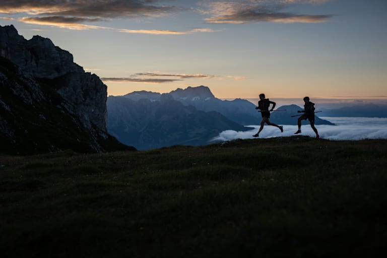 Zwei Trailrunner laufen im Morgengrauen am Berg.