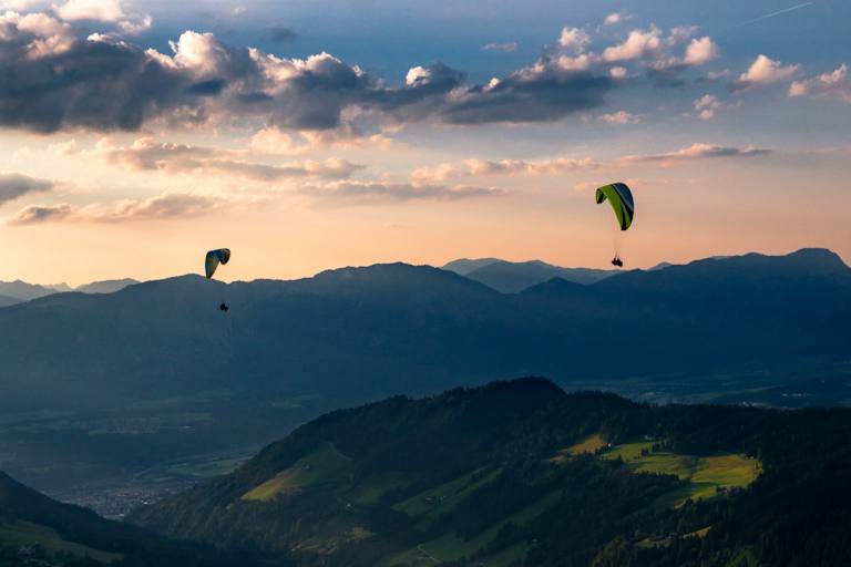 Zwei Personen paragleiten über ein Tal in der Wildschönau.
