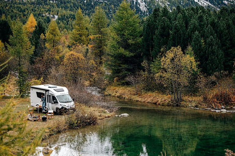 Ein Paar neben einem Van im Wald in der Natur vor einem Teich.