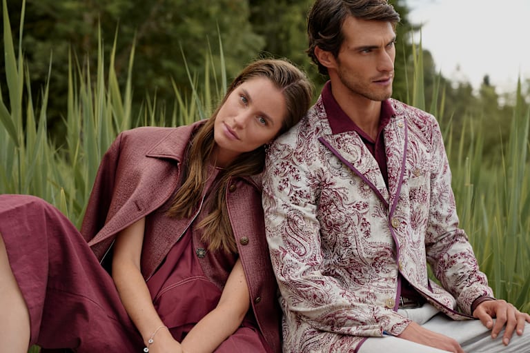 Ein Mann und eine Frau im Freien bei einem See in modischer Kleidung in Rottönen.