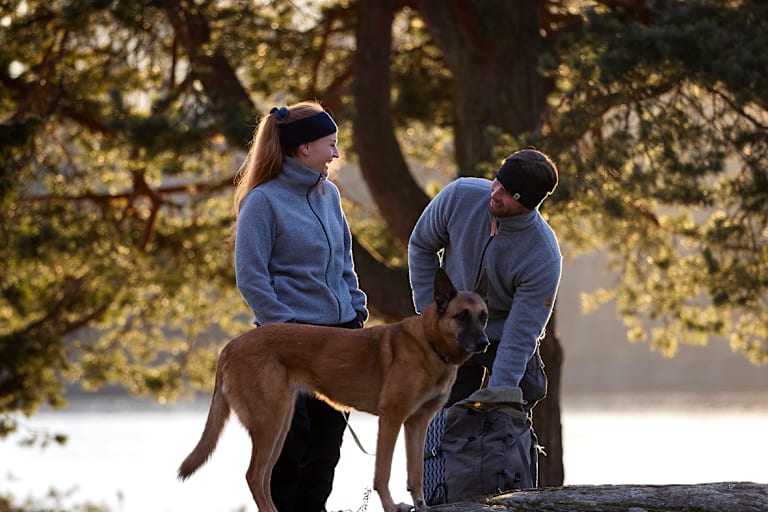Ein Paar in Sportkleidung aus Merinowolle mit Schäferhund im Park im Herbst.