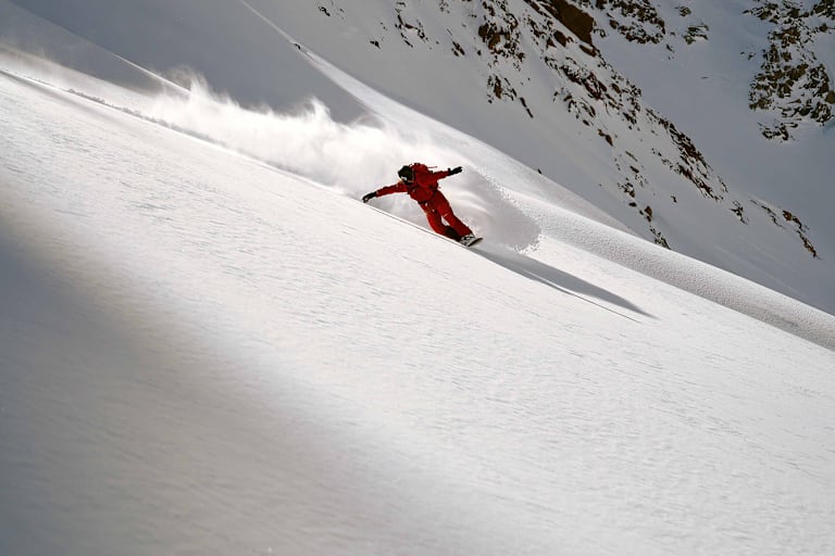 Eine Person fährt Snowboard im Schnee auf einem Berg in roter Ausrüstung.