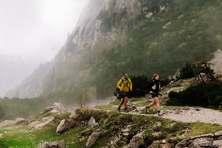 Zwei Läufer im Wald nahe eines Tals im Nebel.