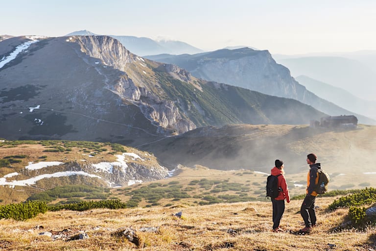 Zwei Wanderer stehen im Herbst auf dem Raxplateau und blicken in die Ferne