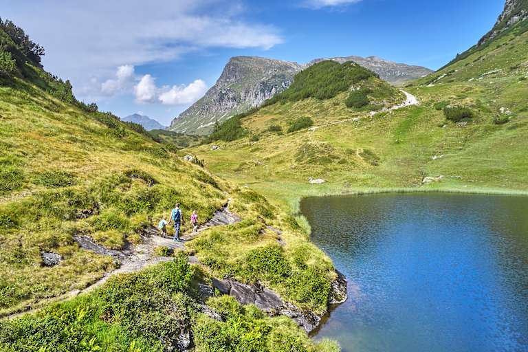 Drei Wanderer wandern an einem Bergsee entlang.