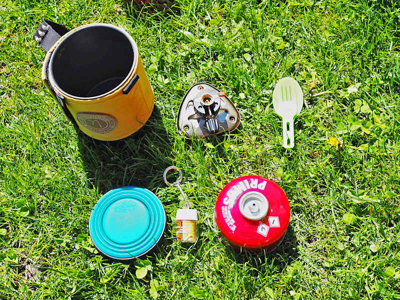 Kocher mit integrierter Kartusche, faltbarem Becher, Besteck und Gewürze.