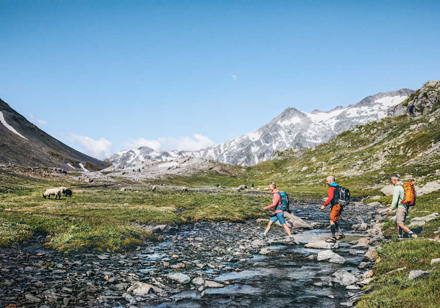 Drei Wanderer gehen über einen Bachlauf.