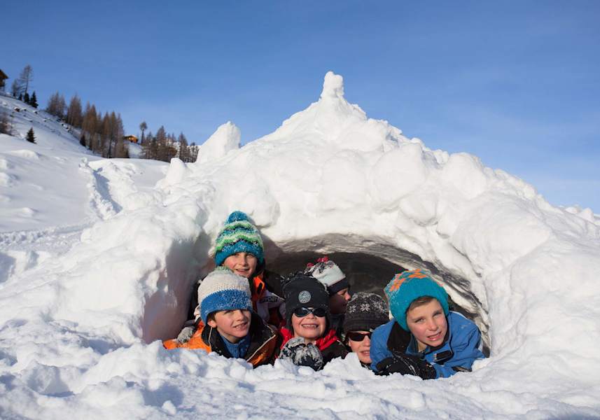 Die Kinder schauen grinsend aus ihrem selbstgebauten Iglu heraus.