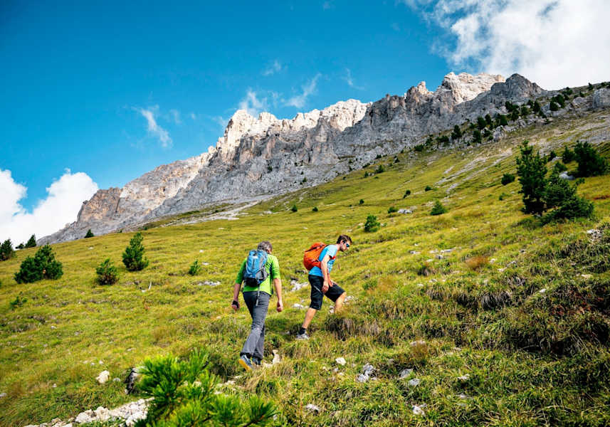 Wanderer steigen über saftige Wiesen auf zu den schroffen Felsen