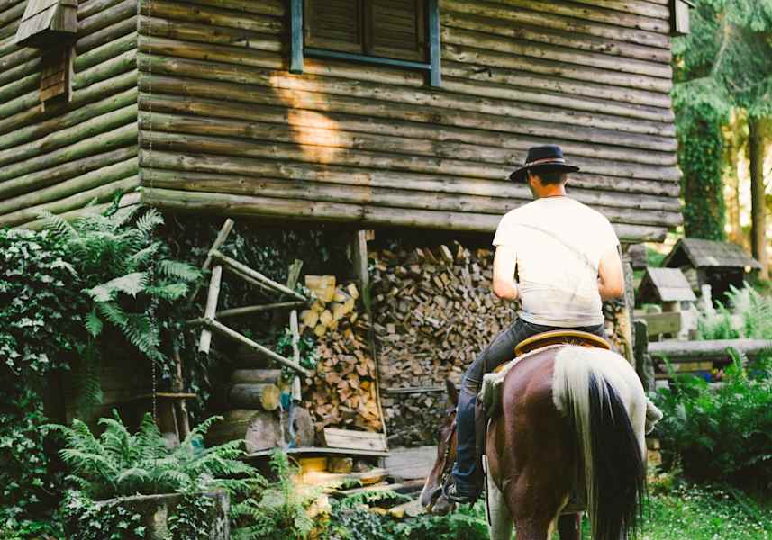 Ein Mann auf seinem Pferd vor einem Blockhaus