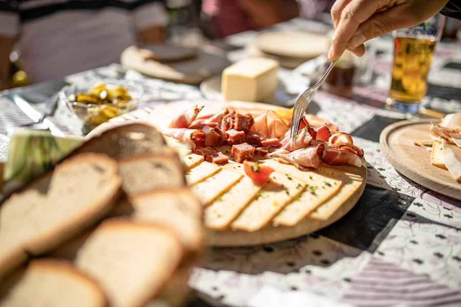 Eine Person nimmt sich Speck von einer typischen Brettljausn.