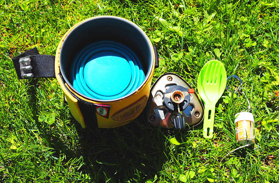 Kocher mit integrierter Kartusche, faltbarem Becher, Besteck und Gewürze.