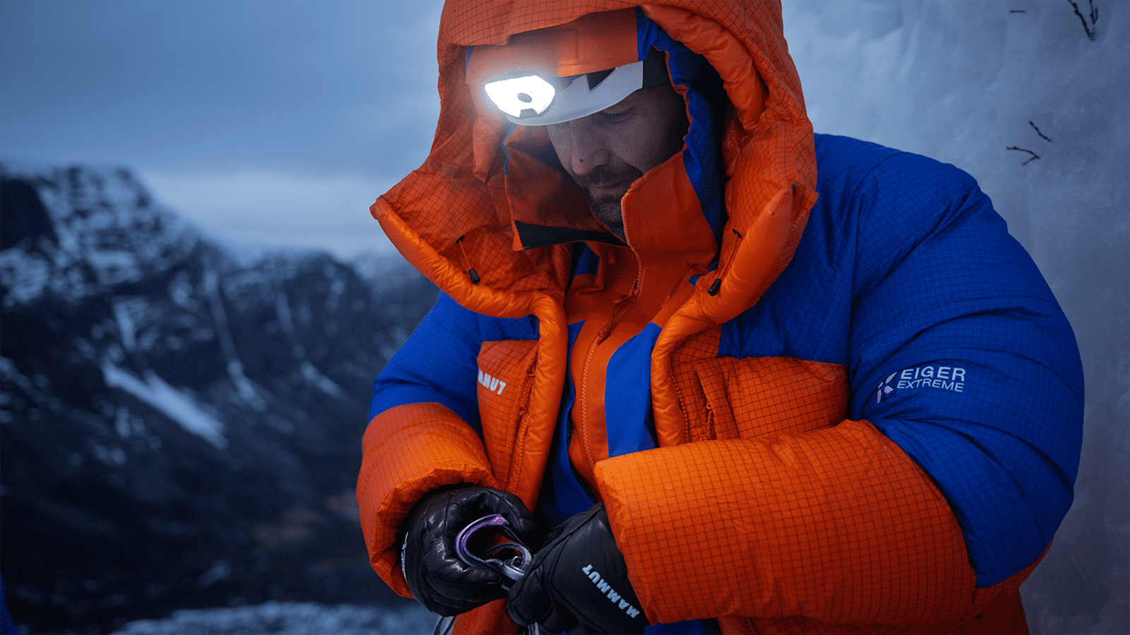 Ein Alpinist steht in den schneebedeckten Bergen und ist mit der neuen Eiger Extreme Nordwand 6.0 Kollektion von Mammut ausgestattet. Über seinem Helm trägt er eine Stirnlampe.