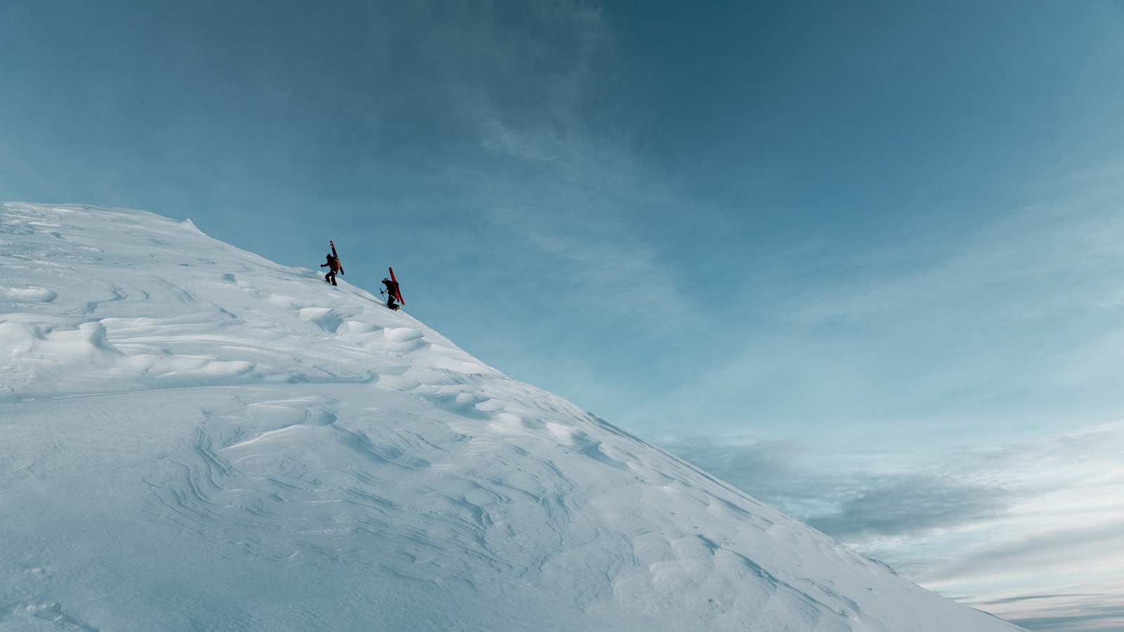 Zwei Skitourengeher gehen einen unberührten Schneehang hinauf.