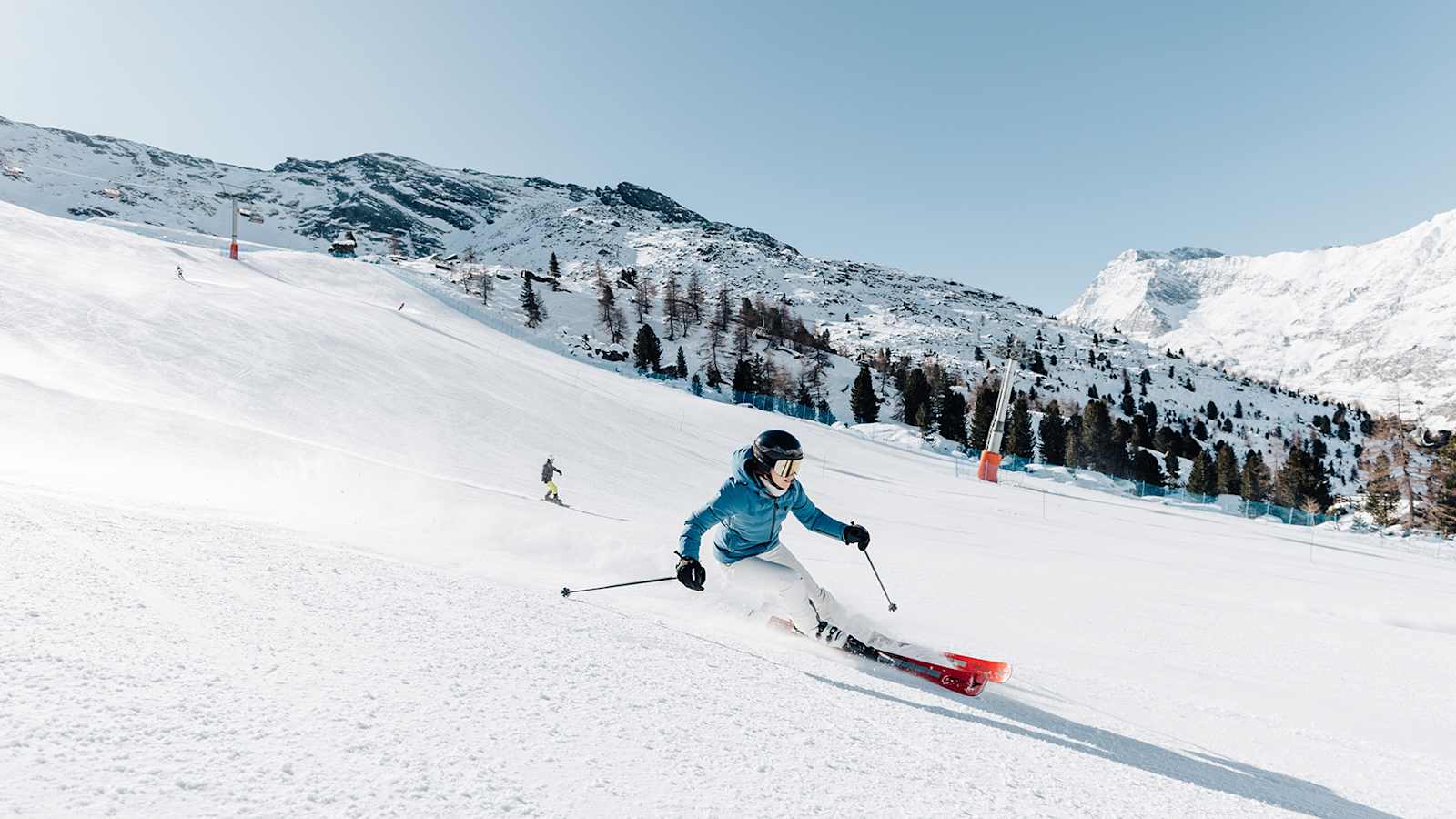 Eine Frau fährt eine Skipiste in der Meraner Bergwelt hinunter. Die Landschaft ist tiefverschneit.