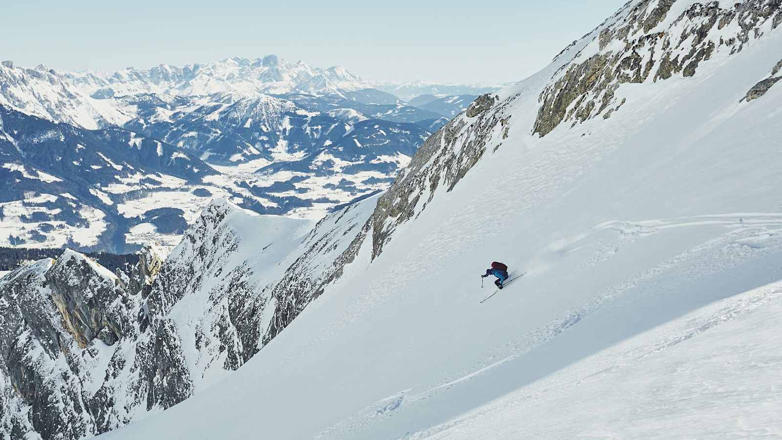 Ein Skifahrer bei der Abfahrt in einer Rinne, dahinter der Alpenhauptkamm.