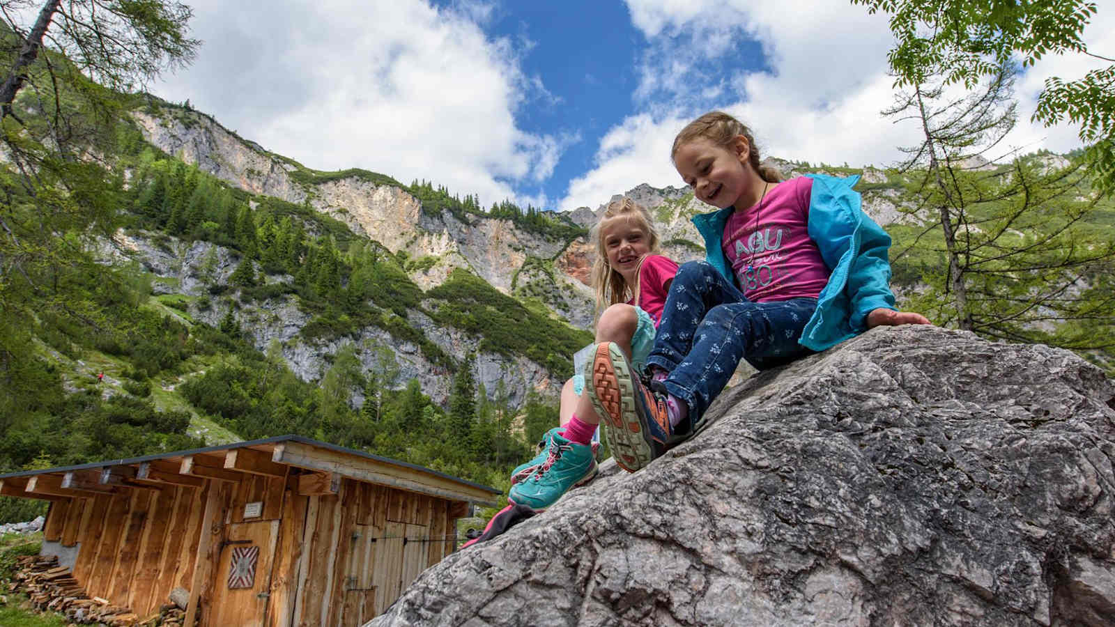 Zwei Mädchen sitzen auf einem Felsen und lächeln in die Kamera.