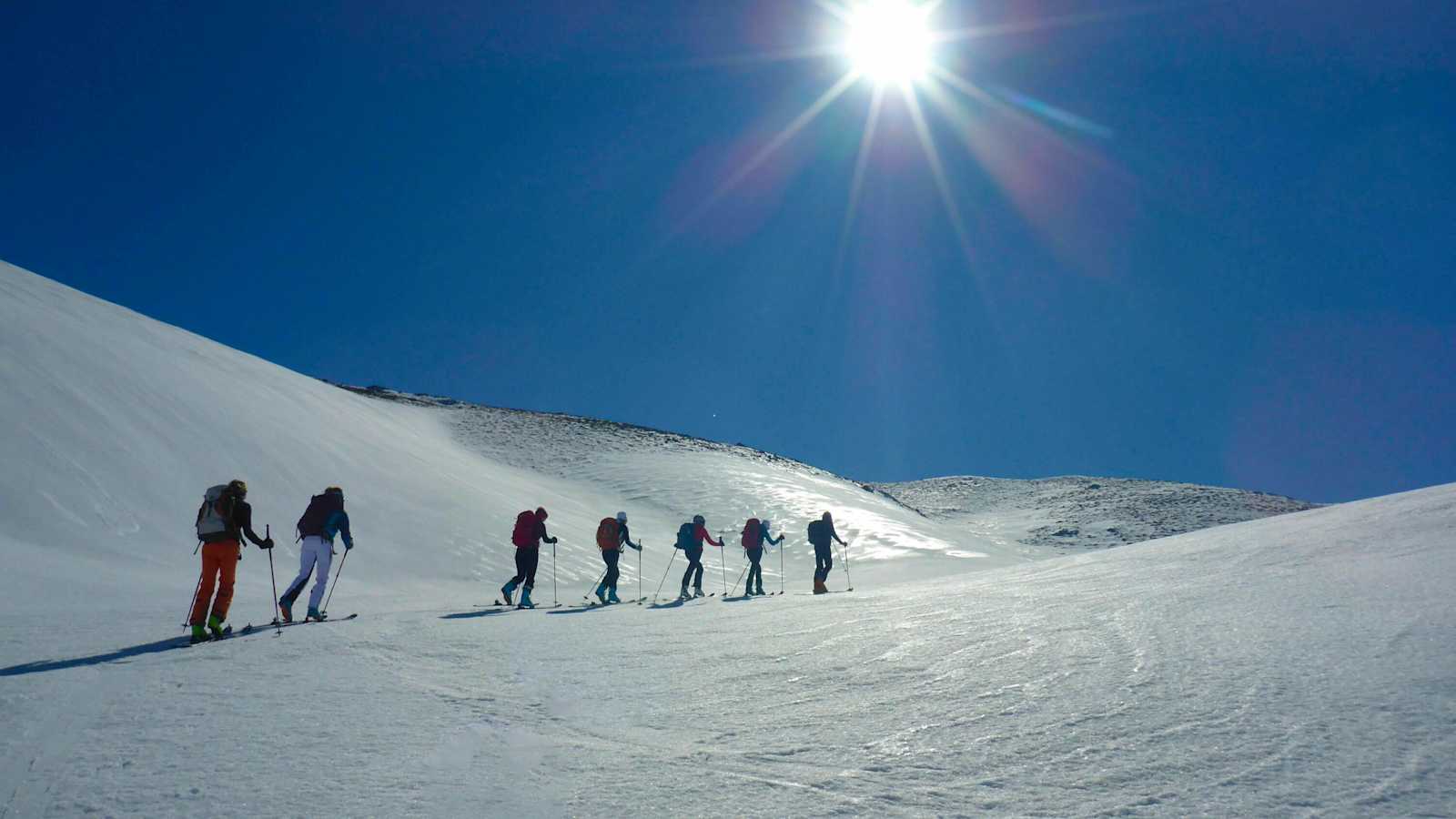 Ein Gruppe von Skitourengehern auf einem Firnspiegel: Die glänzende Spiegelfläche reflektiert das Sonnenlicht