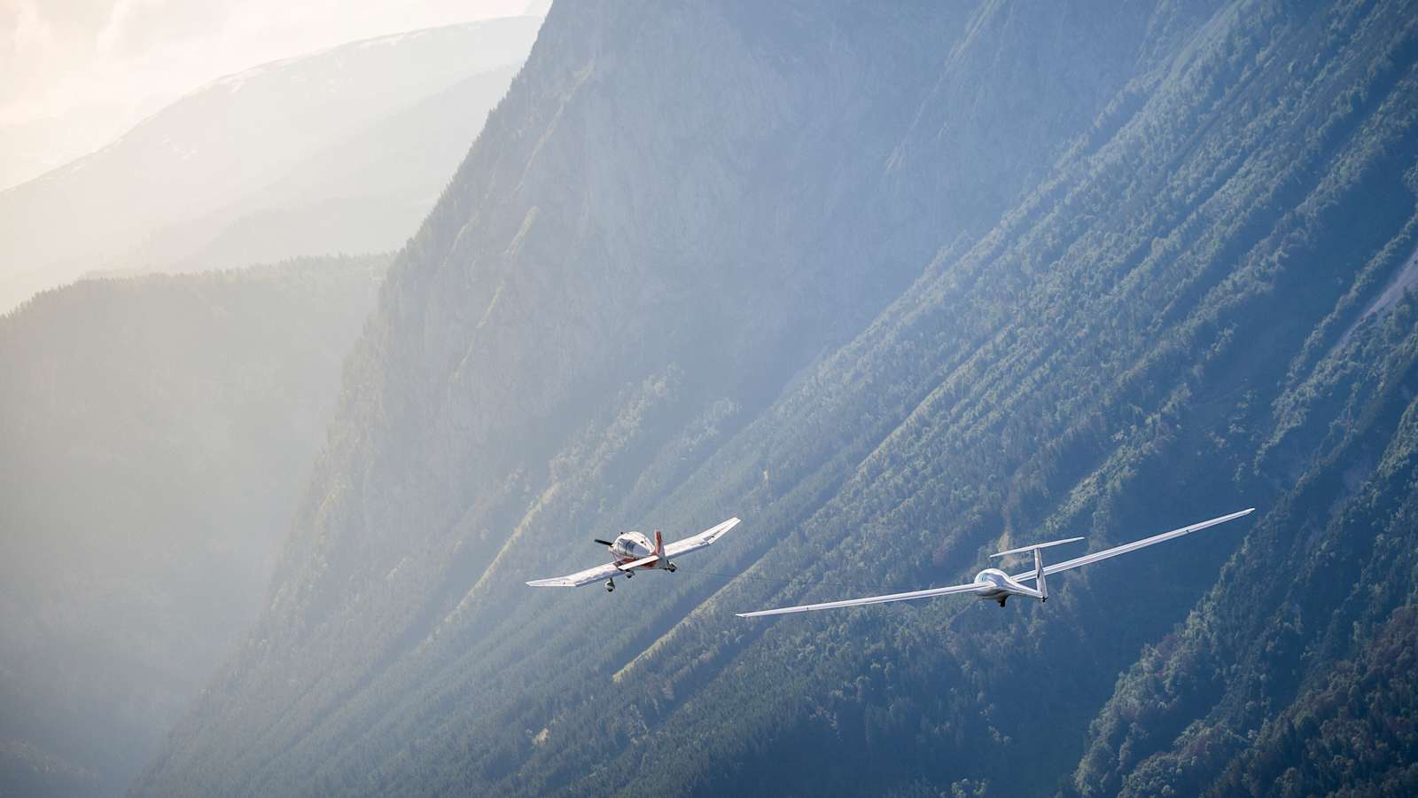 Zwei Flugzeuge vor nebelverschleierten Bergen.