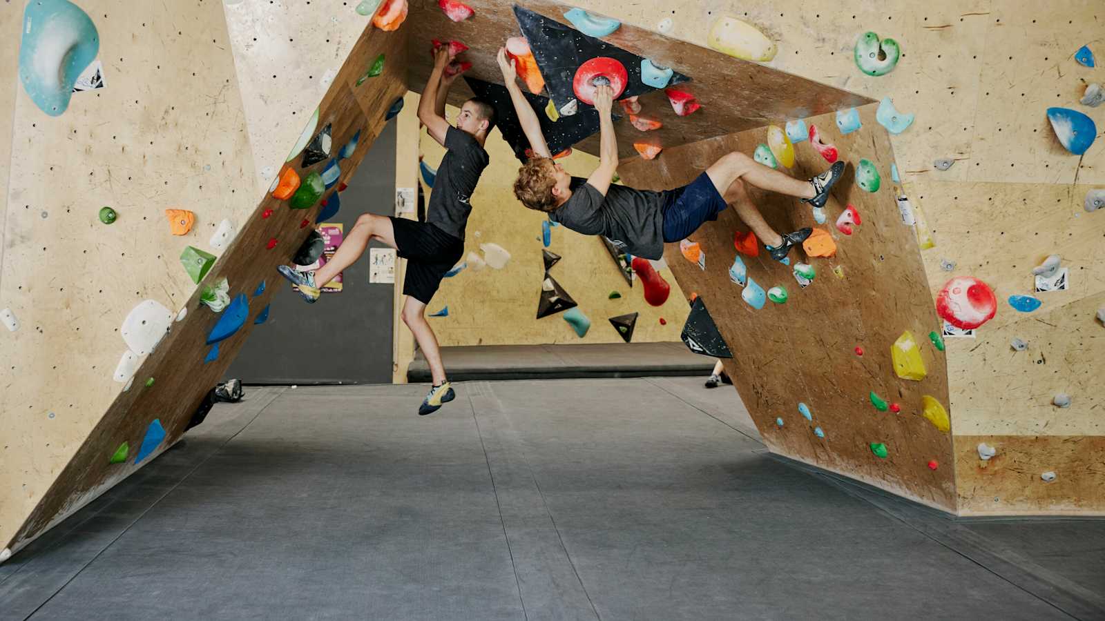 Zwei Boulderer hängen in der Halle an bunten Griffen