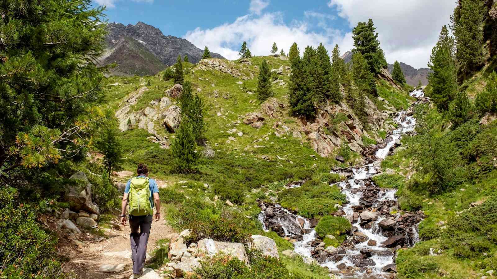 Ein Bergsteiger geht neben einem Bach entlang.