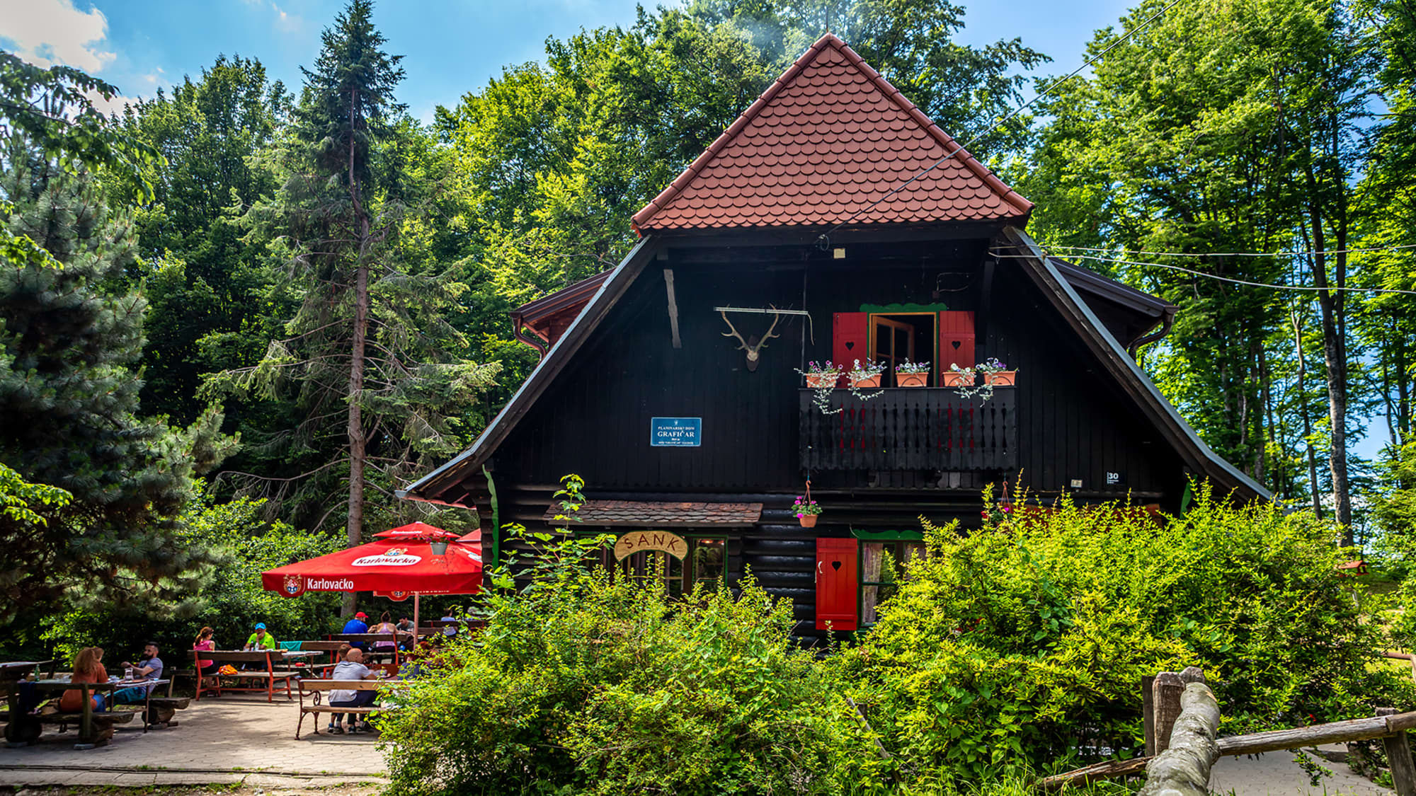 Eine dunkle Holzhütte im Wald, welche als Gasthaus dient und Menschen bedient.