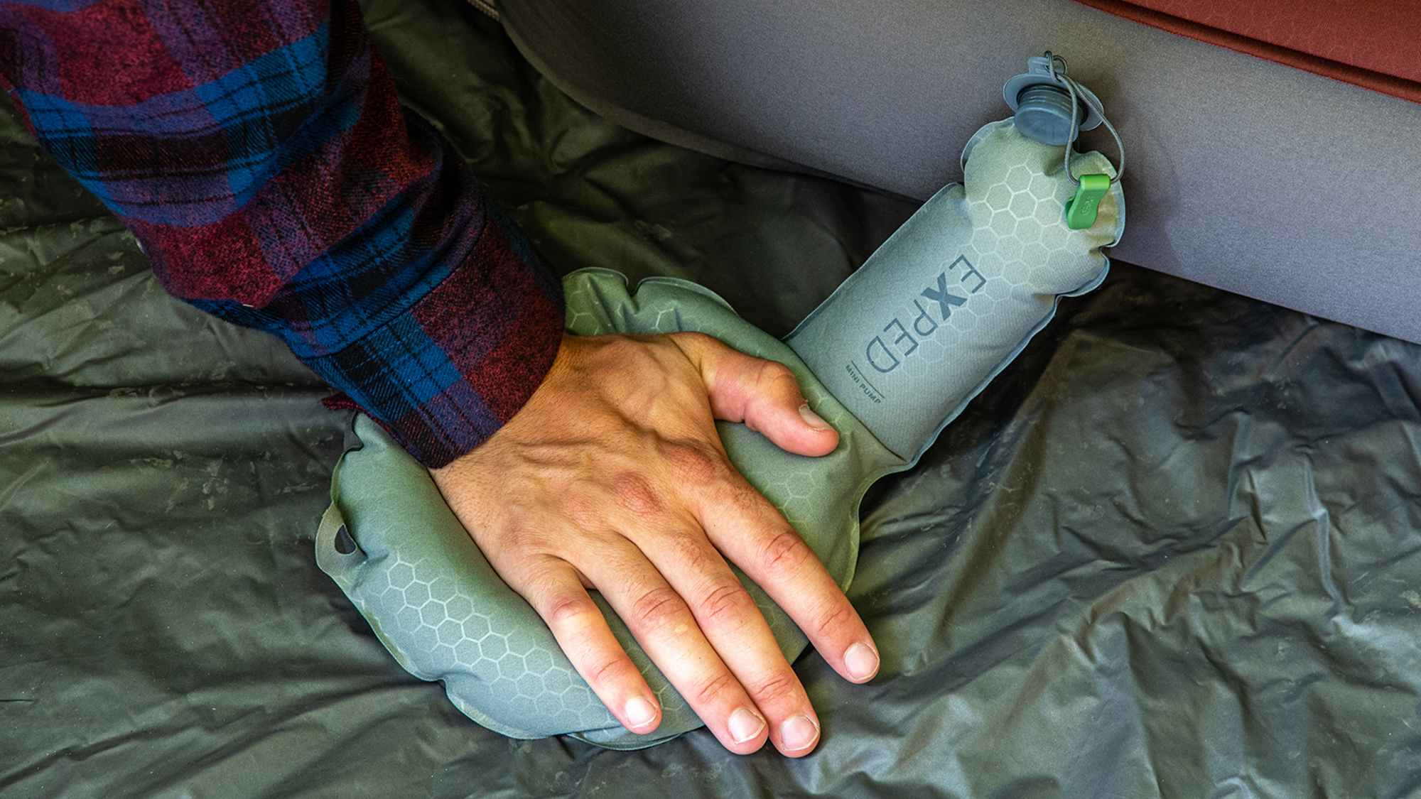 Eine Hand drückt auf die Mini Pump von Exped, um eine Schlafmatte aufzublasen.