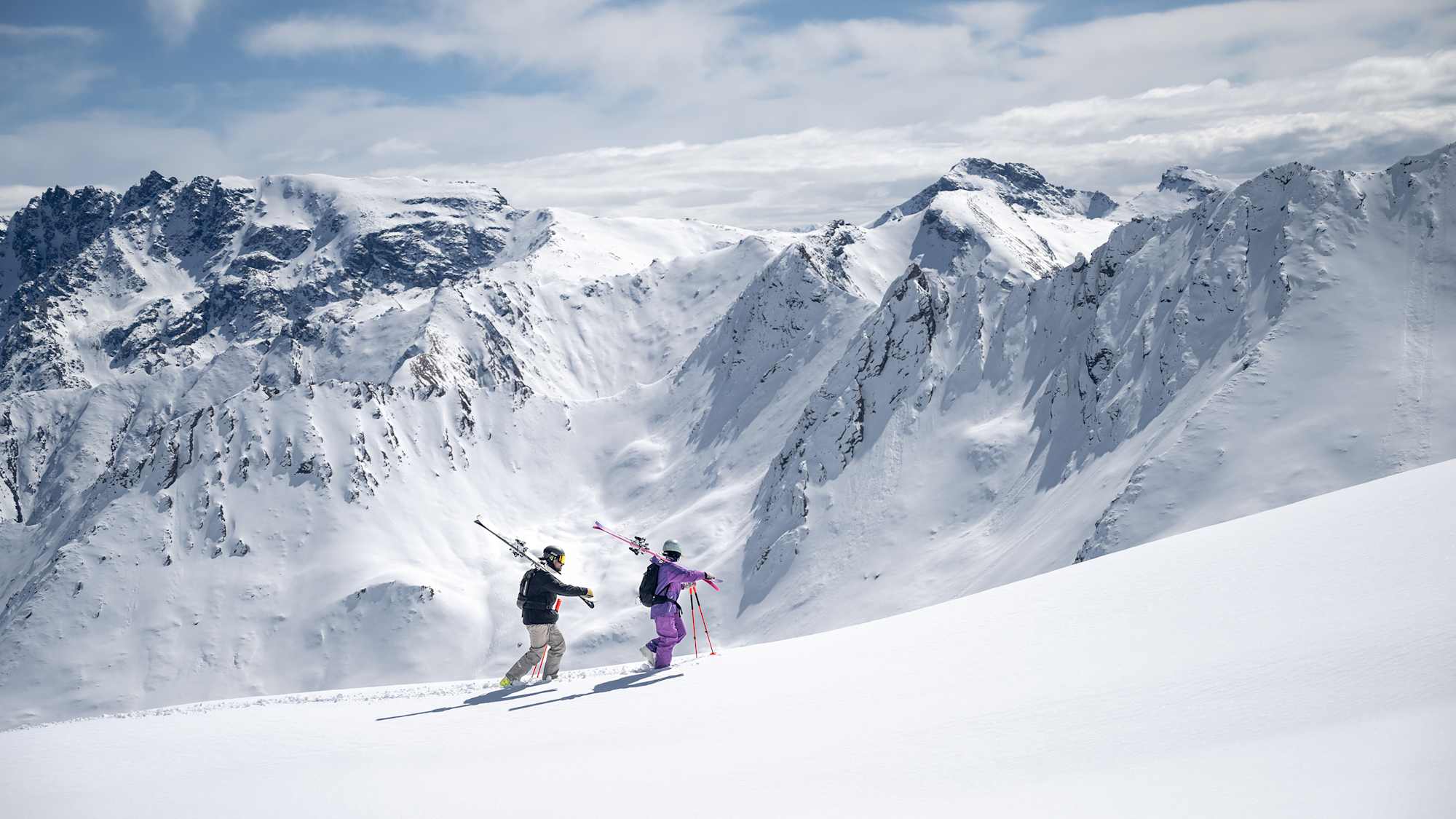 Zwei Freerider gehen einen unberührten Schneehang entlang.