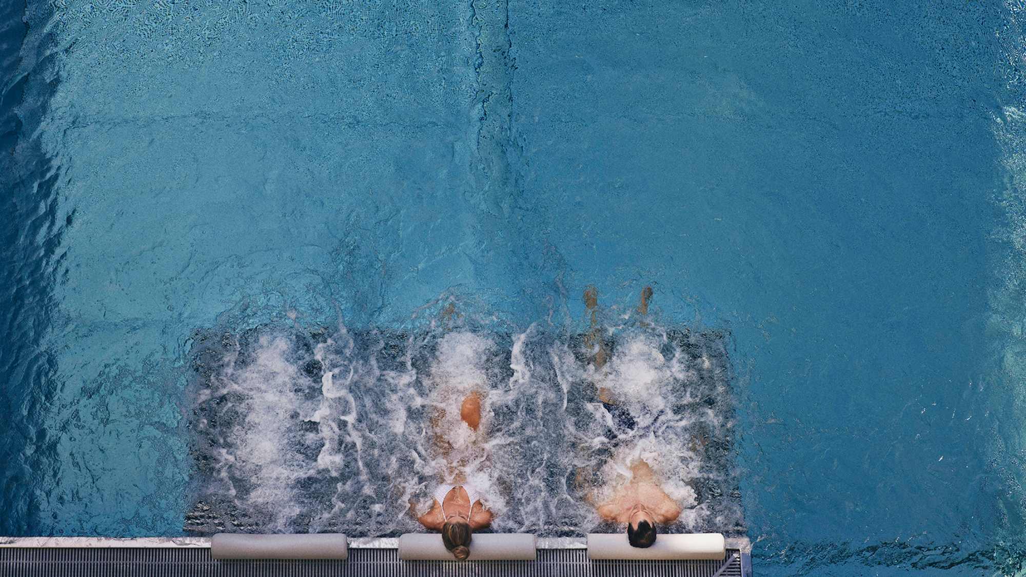 Zwei Personen liegen nebeneinander auf Liegen im Pools vom Hotel Guglwald und genießen die Ruhe am Wasser.