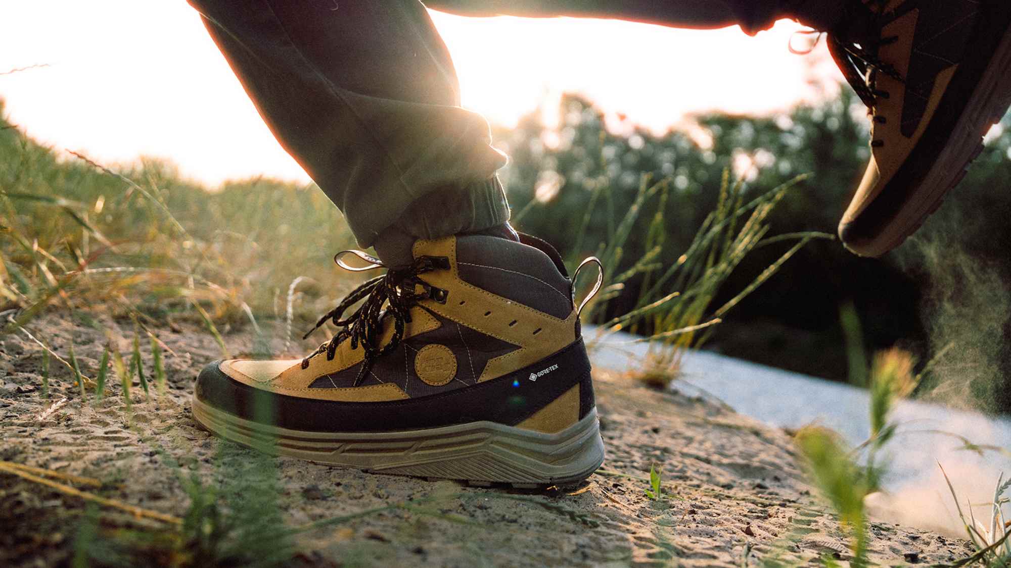 Nahaufnahme eines Hanwag Rotpunkt Light Mid GTX Wanderschuhs auf unbefestigtem Weg bei Sonnenuntergang – robuster, wasserdichter Outdoor-Schuh mit GORE-TEX-Membran.