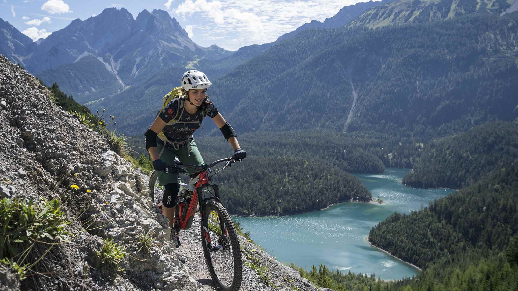 Eine Frau fährt mit ihrem Fahrrad entlang einer Radstrecke entlang und wird dabei von einem spektakulären Panorama begleitet.