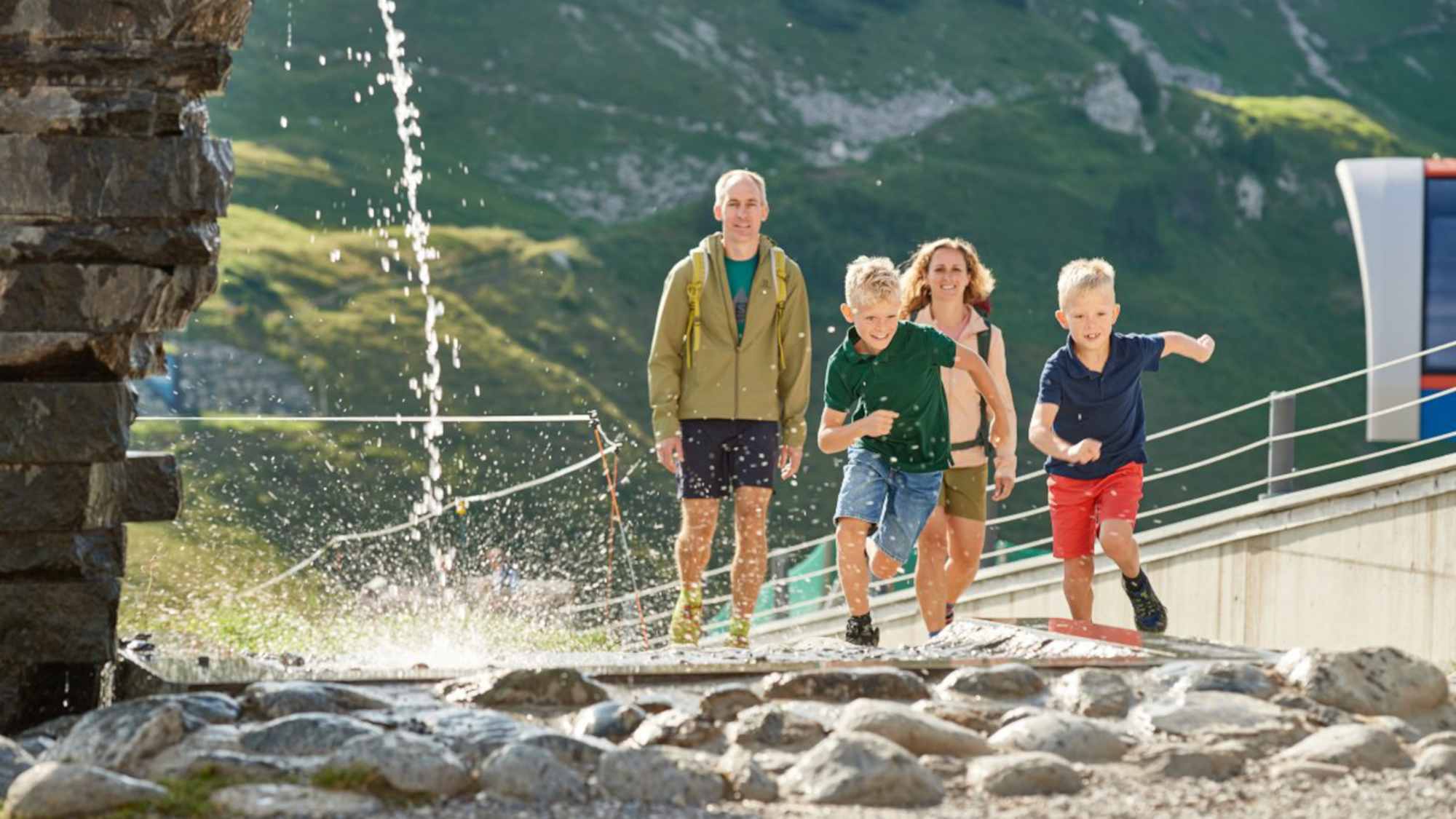 Eine Familie läuft einem plätscherndem Wasserstrahl entgegen.