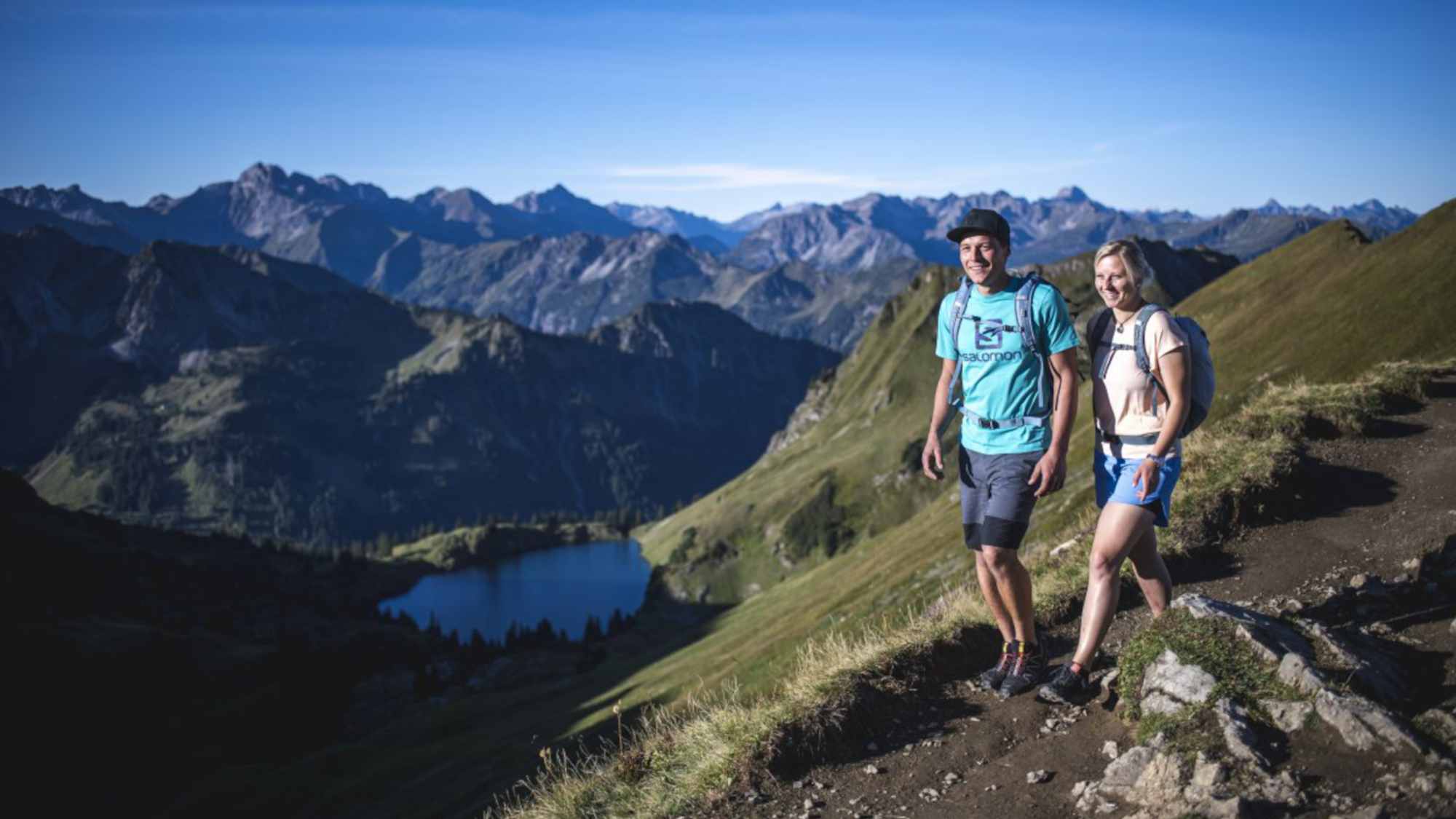 Zwei Wanderer vor einer schönen Berglandschaft mit einem blauen See.