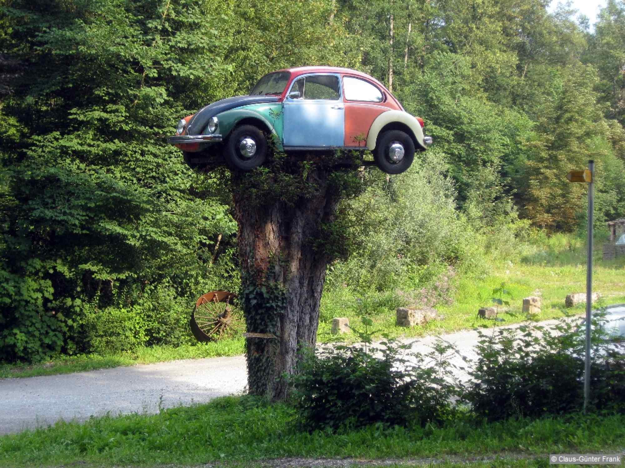 VW-Käfer auf einem Baumstumpf vor einer Lackiererei