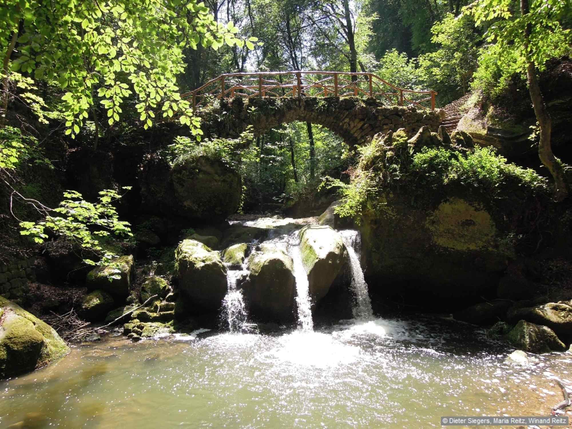 Der Wasserfall mit drei Kaskaden, über den sich eine Steinbrücke schwingt, liegt mitten im wildromantischen Müllerthal (franz. Mullerthal).