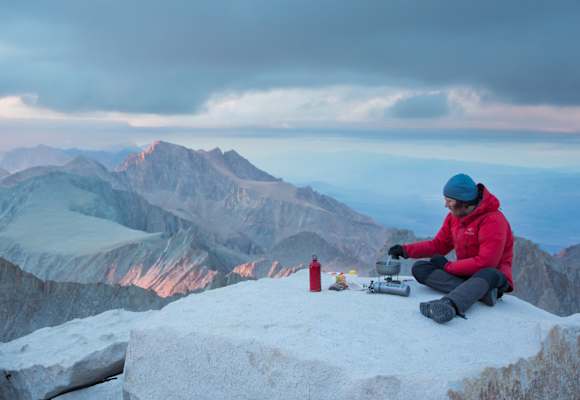 Mann kocht mit SOTO Kocher auf Berg Essen mit Panorama über Berge.