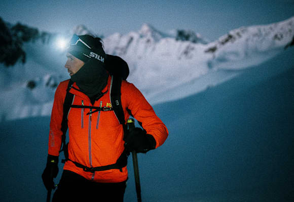 Ein Mann geht im Schnee und Skiausrüstung in der Nacht mit einer Stirnlampe skifahren.
