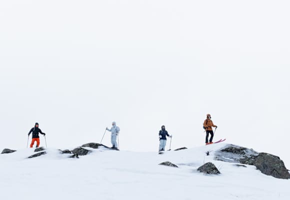 Vier Skifahrer stehen auf einen Gipfel und tragen robuste und moderne Outdoor-Kleidung.